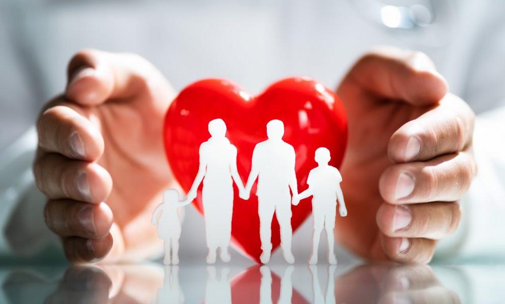 Paper cutouts of four people: two adults and two children, in front of a red heart with hands surrounding the heart